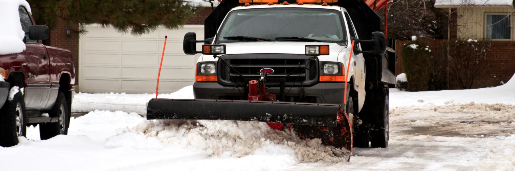 Pickup truck with a snow plow clearing a residential driveway